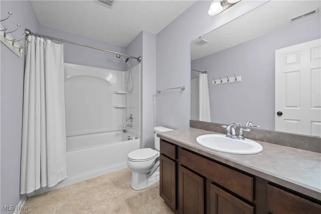 Bathroom featuring a textured ceiling, shower / tub combo, and vanity