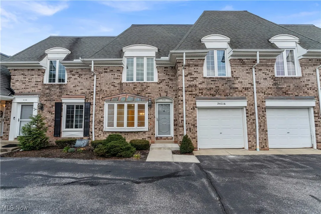 View of front of home featuring roof with shingles, driveway, brick siding, and a garage