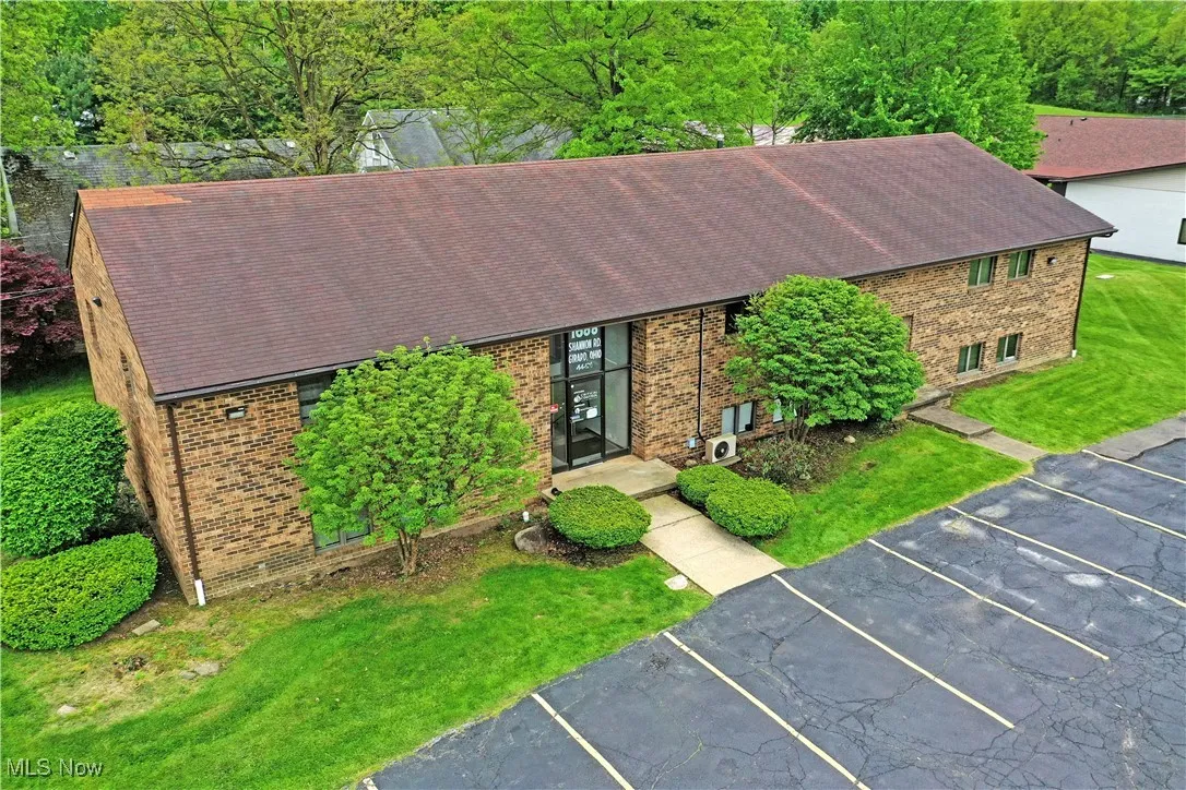 View of front facade featuring a shingled roof, uncovered parking, brick siding, and a front lawn