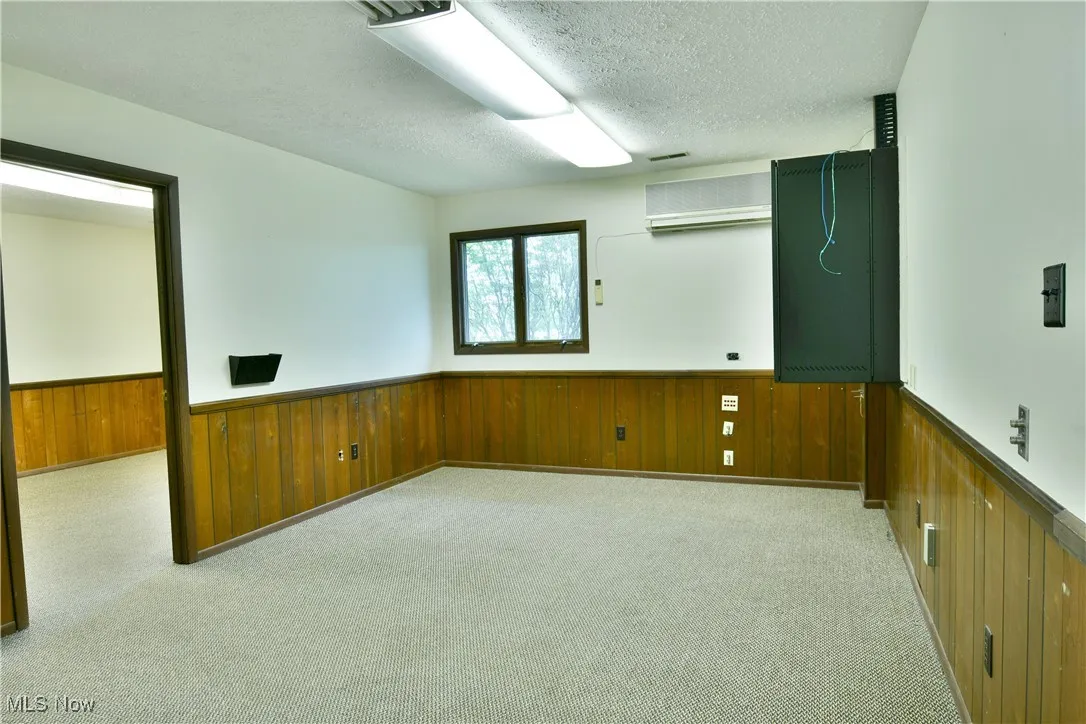 Carpeted empty room featuring wooden walls, wainscoting, a wall unit AC, and a textured ceiling