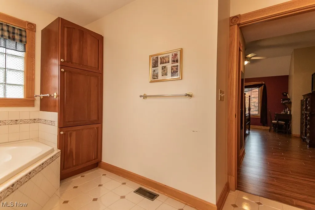 Full bath featuring a garden tub and light tile and storage cabinet