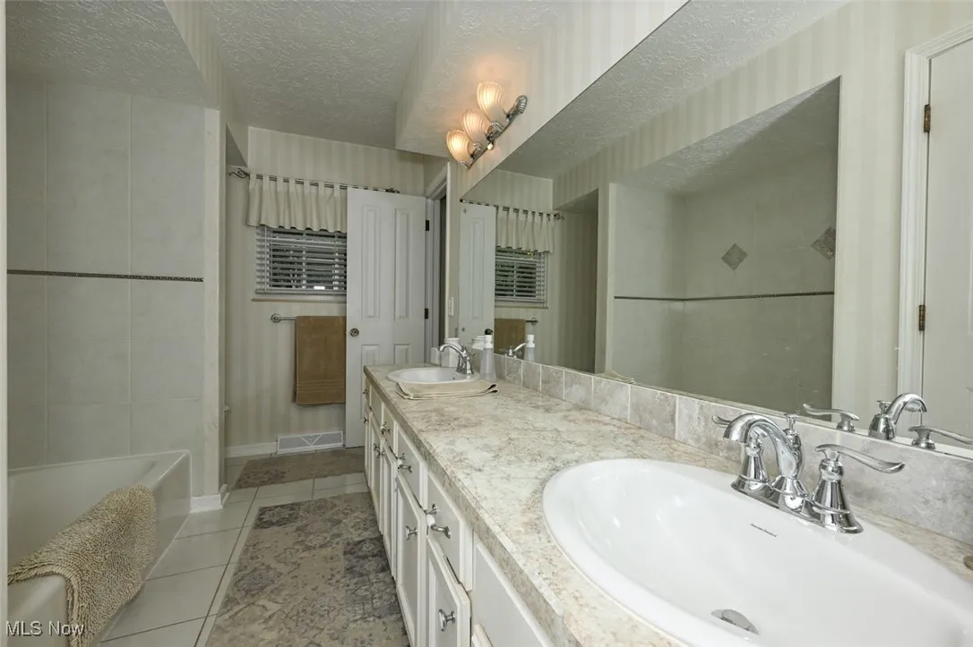 Full bath with a textured ceiling, light tile patterned floors, double vanity, and shower / bath combo
