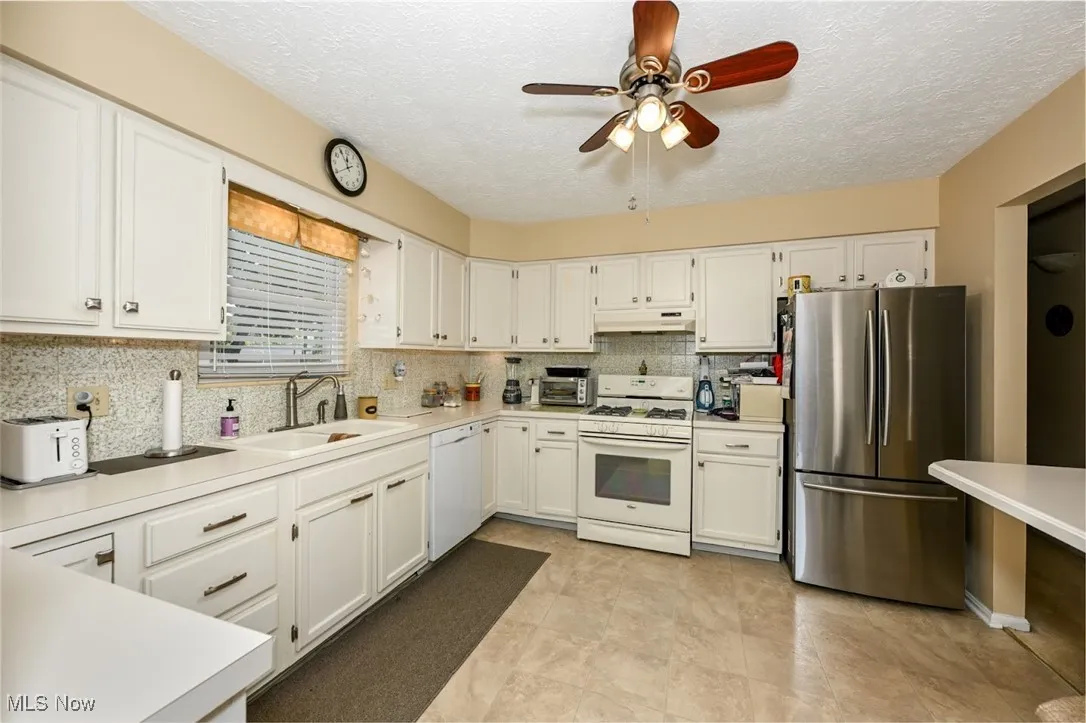 Kitchen featuring white appliances, light countertops, white cabinets, and a textured ceiling