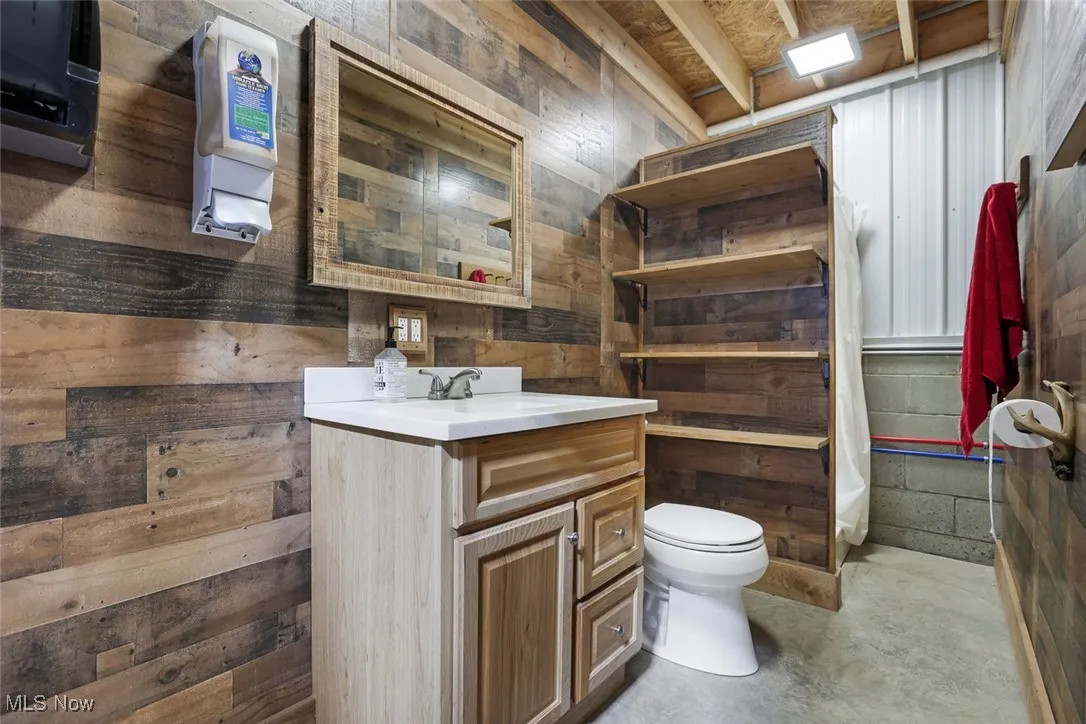 Bathroom with vanity, wooden walls, and unfinished concrete floors