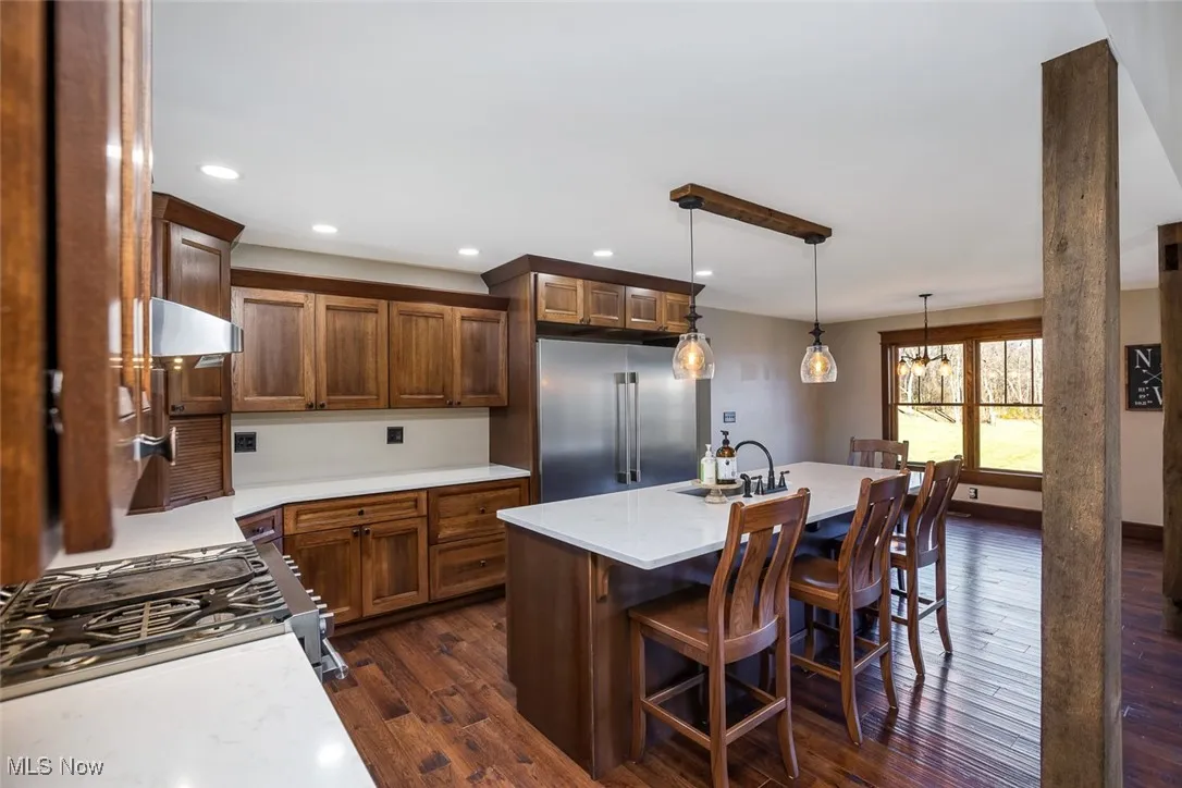 Kitchen featuring a center island with sink, stainless steel appliances, pendant lighting, dark wood-style flooring, and a kitchen breakfast bar