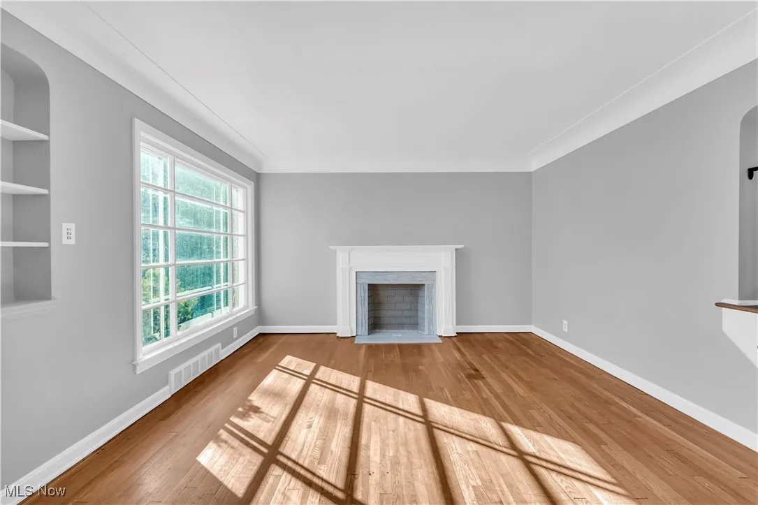 Unfurnished living room featuring light wood-style floors, a fireplace with flush hearth, crown molding, and arched walkways