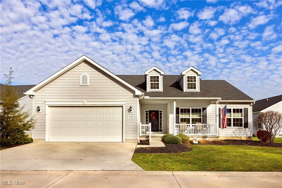 View of front facade with a porch, roof with shingles, driveway, a front yard, and a garage