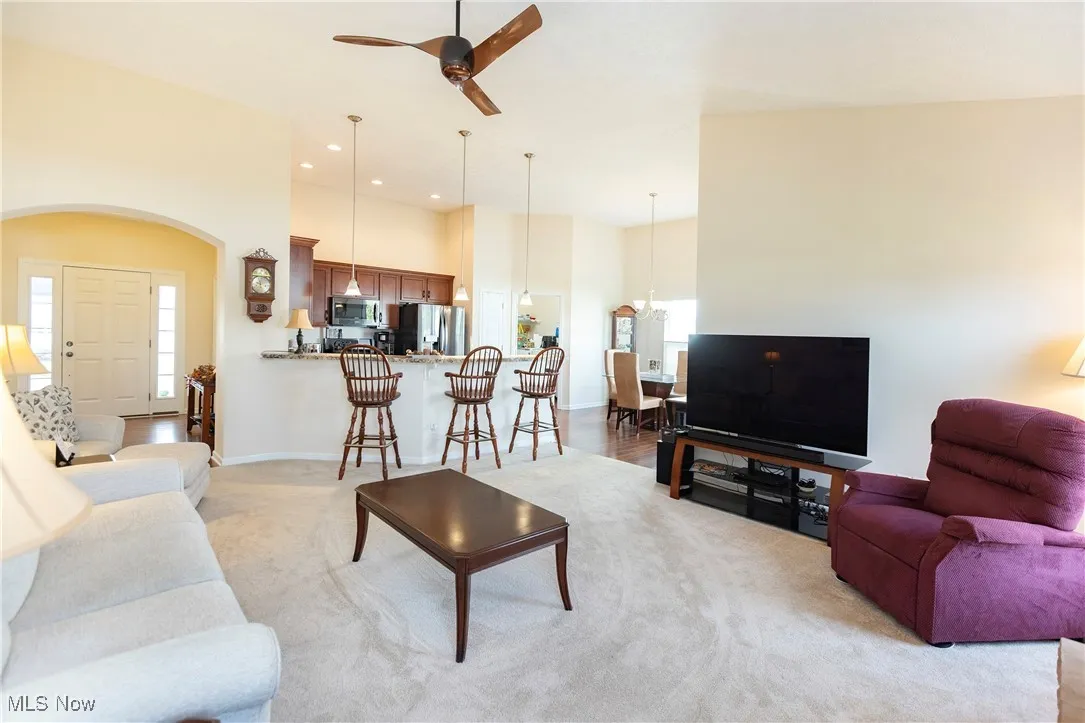 Living room with arched walkways, light colored carpet, ceiling fan, plenty of natural light, and a towering ceiling