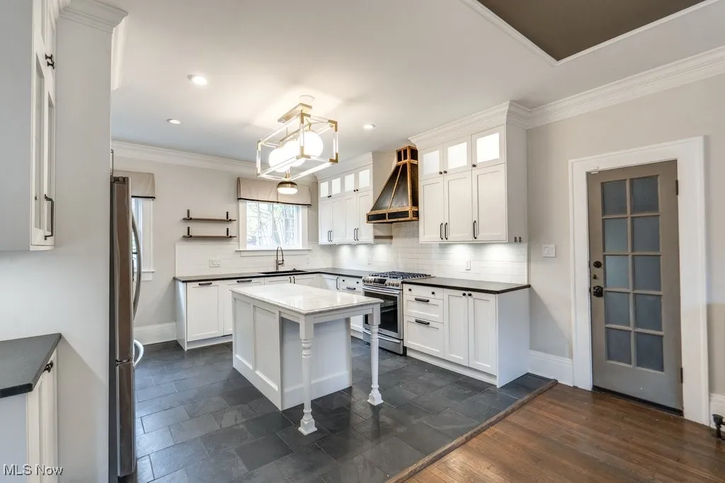 Kitchen with ornamental molding, open shelves, white cabinetry, appliances with stainless steel finishes, and premium range hood