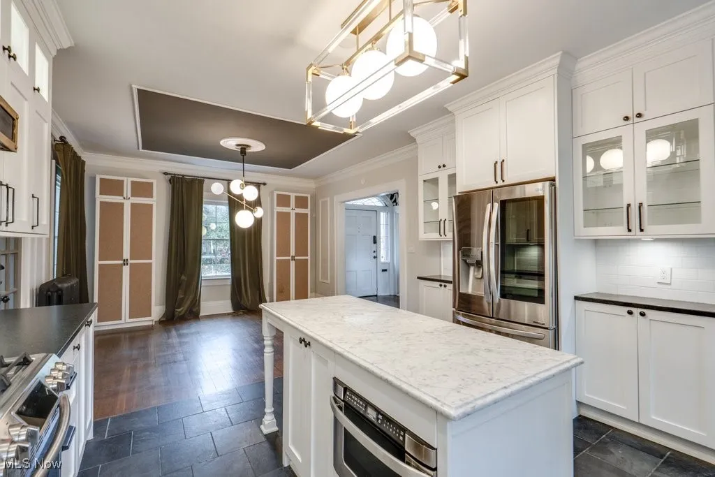 Kitchen featuring decorative light fixtures, dark countertops, white cabinets, stainless steel appliances, and a chandelier
