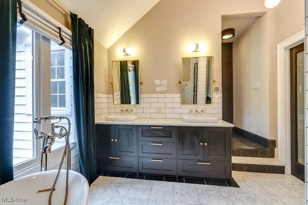 Bathroom featuring tasteful backsplash, healthy amount of natural light, vaulted ceiling, double vanity, and a freestanding bath
