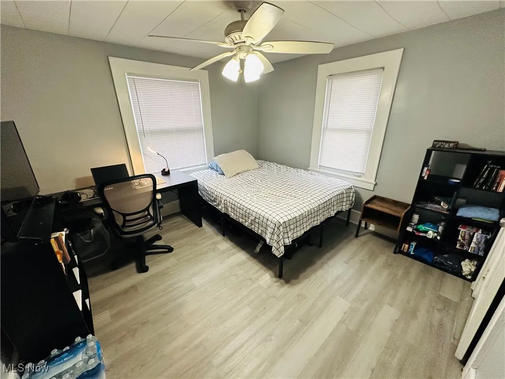 Bedroom with light wood-style floors, a ceiling fan, a desk, and multiple windows