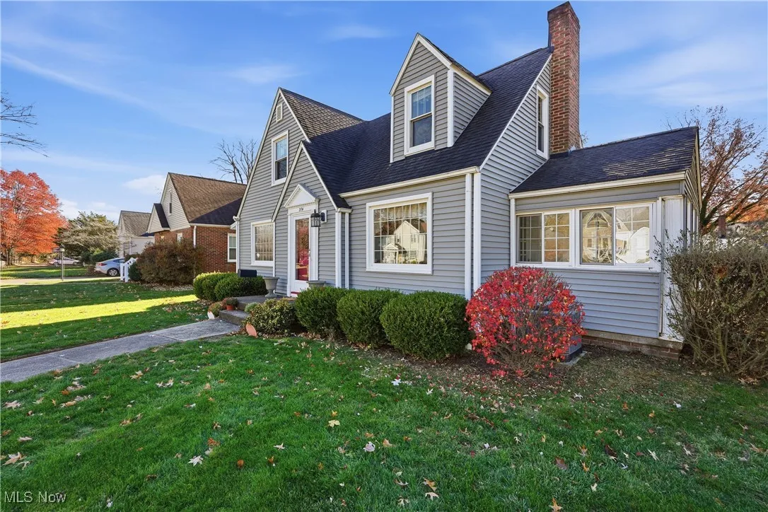 View of front facade featuring a front lawn, roof with shingles, and a chimney