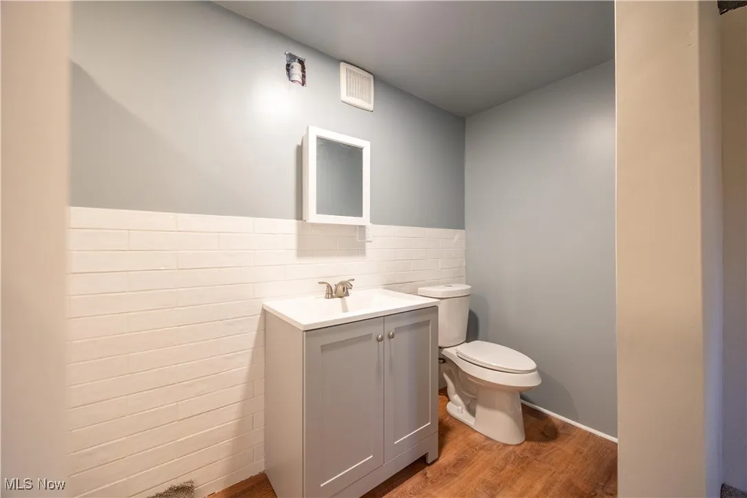Half bath featuring light wood-style floors, vanity, tile walls, and wainscoting