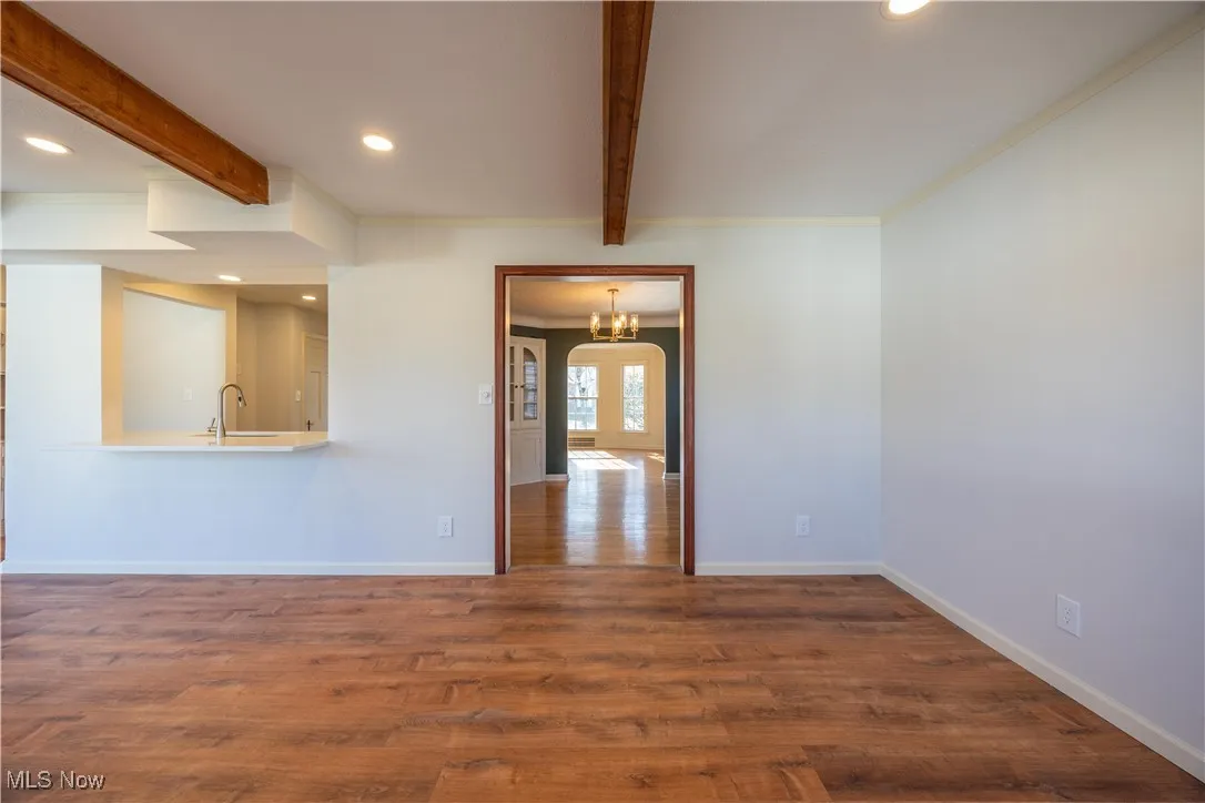 Unfurnished room featuring beam ceiling, dark wood-style floors, recessed lighting, arched walkways, and a chandelier