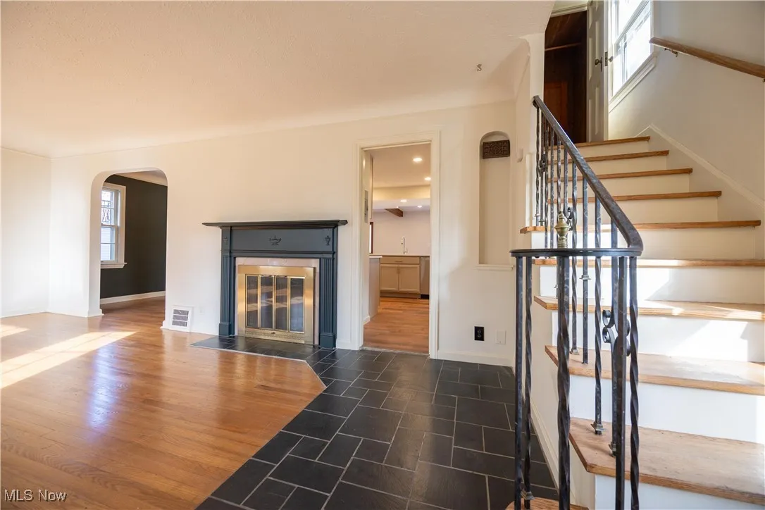 Unfurnished living room with dark wood-style flooring, arched walkways, stairway, a tile fireplace, and recessed lighting