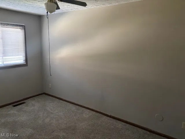 Empty room with a textured ceiling, carpet, and a ceiling fan
