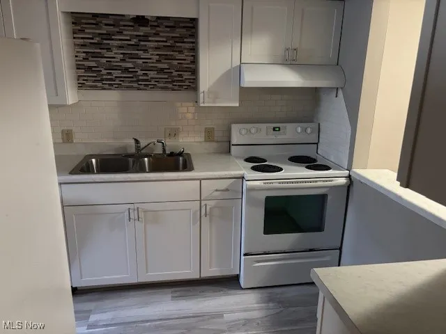 Kitchen with white electric range oven, light countertops, white cabinetry, under cabinet range hood, and tasteful backsplash