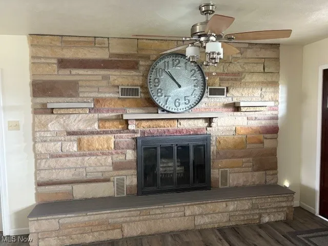 Detailed view of a fireplace, wood finished floors, and ceiling fan