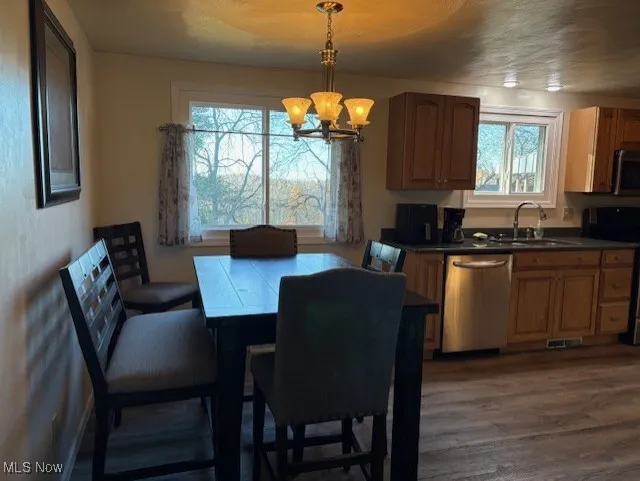 Kitchen featuring dark countertops, stainless steel appliances, a chandelier, brown cabinets, and decorative light fixtures