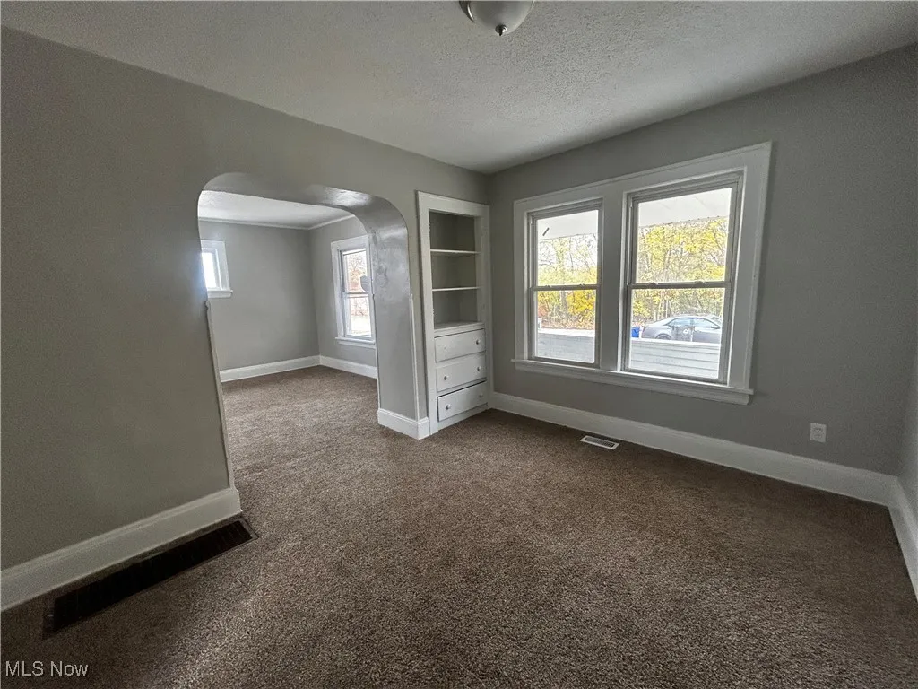 Unfurnished room with dark colored carpet, arched walkways, and a textured ceiling