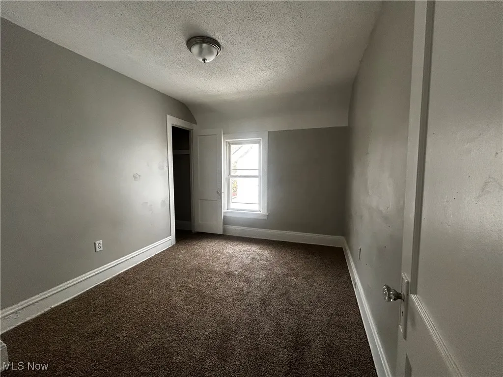 Carpeted empty room with vaulted ceiling and a textured ceiling