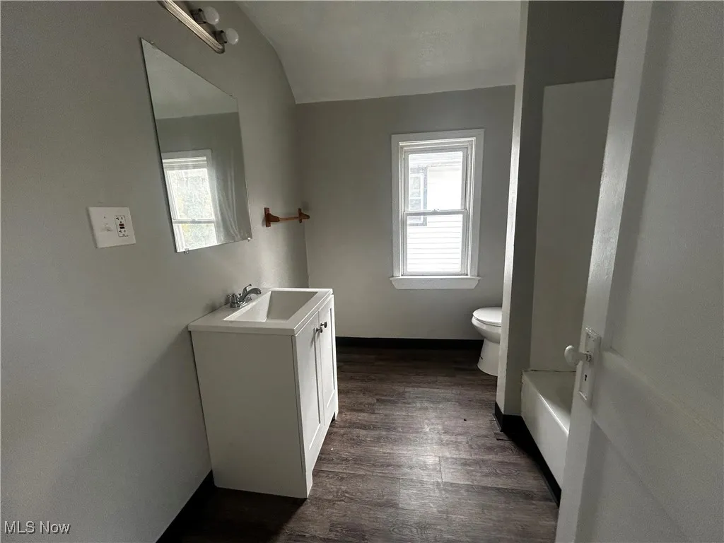 Full bath with vanity, dark wood finished floors, tub / shower combination, and vaulted ceiling