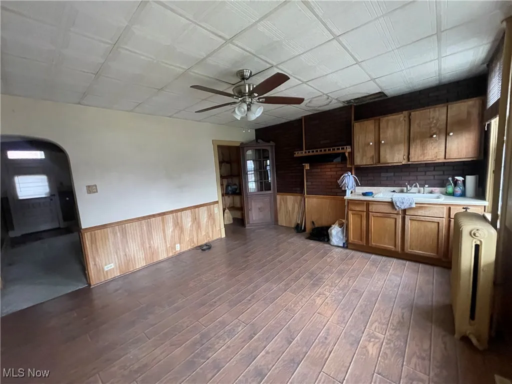 Kitchen featuring a wainscoted wall, light countertops, arched walkways, ceiling fan, and radiator heating unit