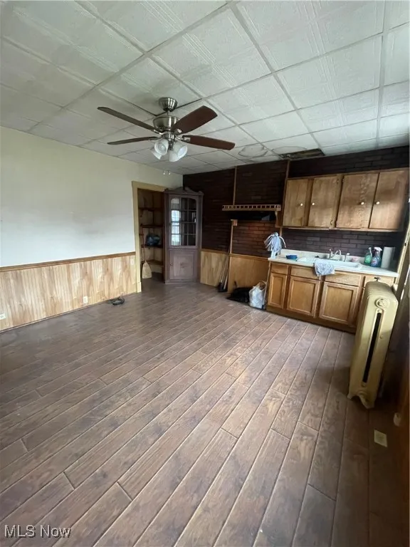 Kitchen with a wainscoted wall, light countertops, brown cabinetry, wood walls, and a ceiling fan