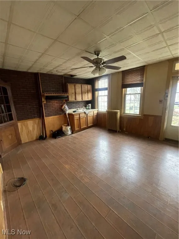 Unfurnished room with a wainscoted wall, wood walls, radiator, dark wood-style floors, and ceiling fan