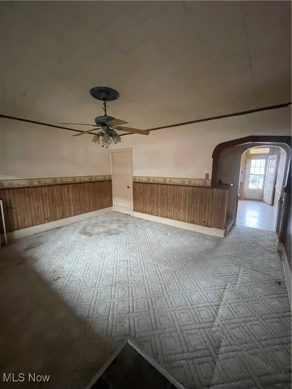Unfurnished room with arched walkways, wainscoting, wooden walls, and ceiling fan