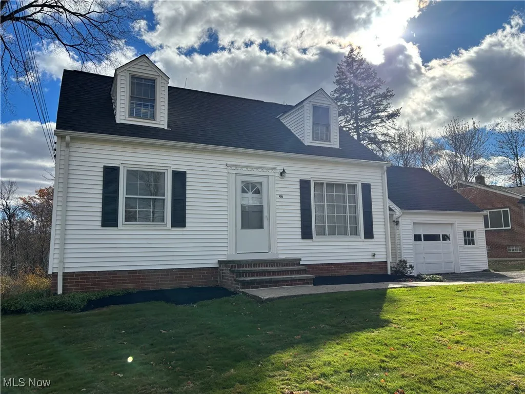 Cape cod-style house featuring entry steps, a front lawn, a garage, and roof with shingles