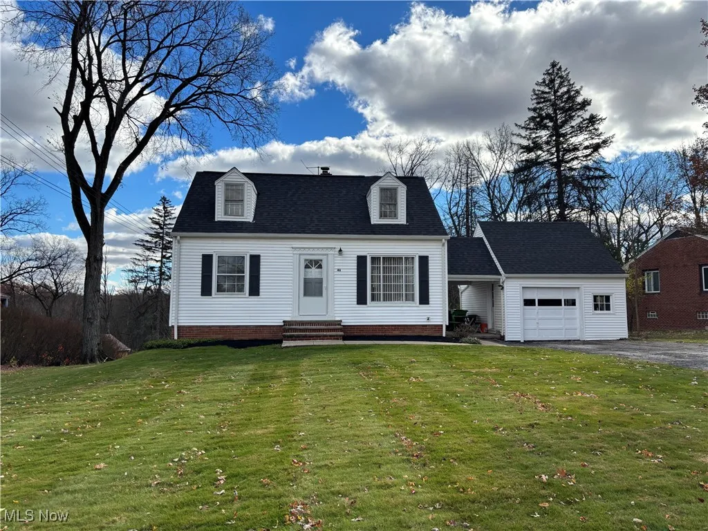 Cape cod-style house featuring a front lawn, an attached garage, entry steps, a shingled roof, and asphalt driveway