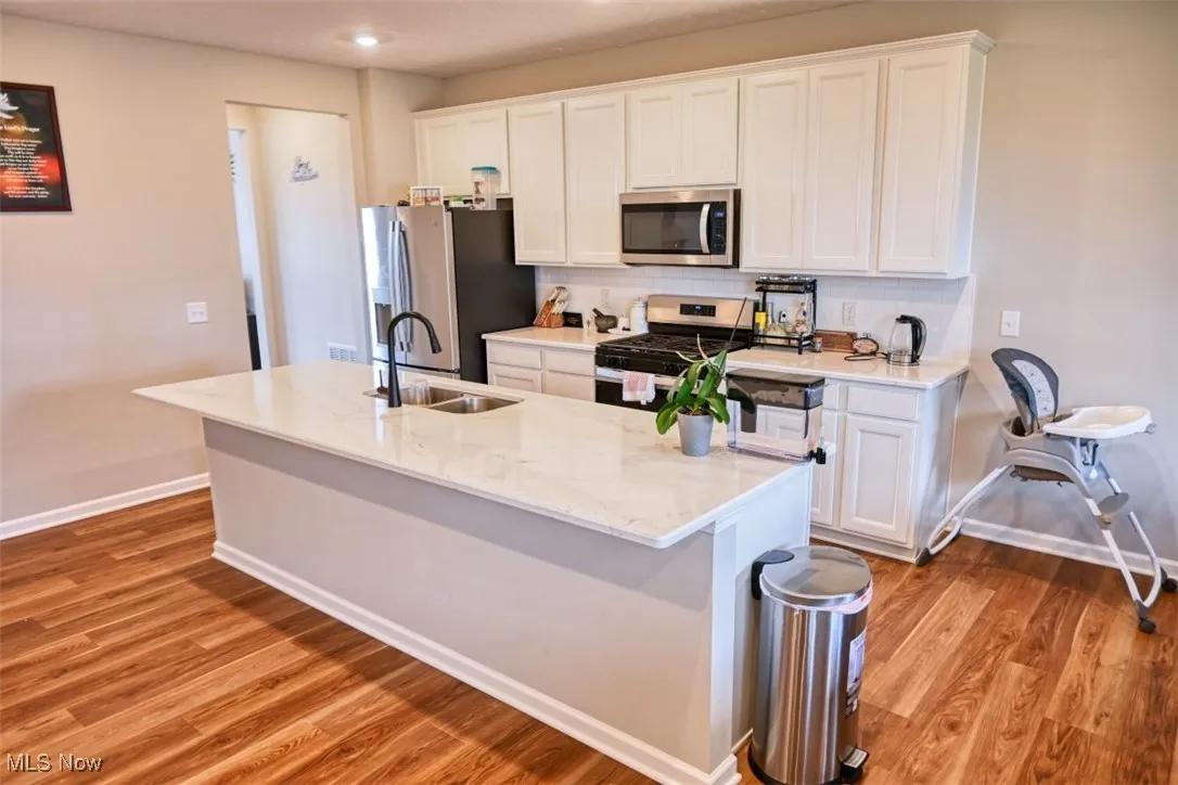 Kitchen with backsplash, white cabinetry, stainless steel appliances, light stone countertops, and recessed lighting
