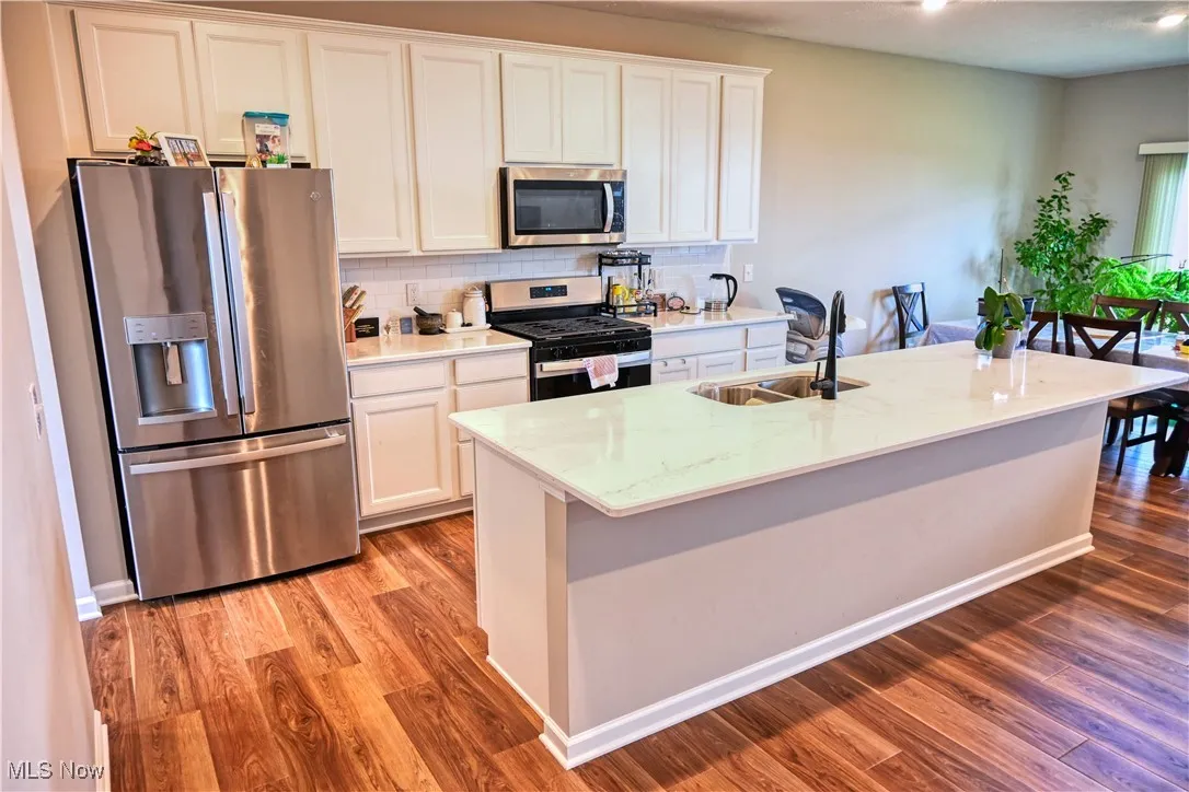 Kitchen with stainless steel appliances, backsplash, light stone counters, and white cabinets