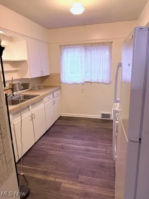 Kitchen with freestanding refrigerator, white cabinets, light countertops, and dark wood finished floors