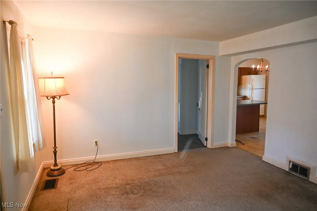 Spare room featuring arched walkways, carpet floors, and a chandelier