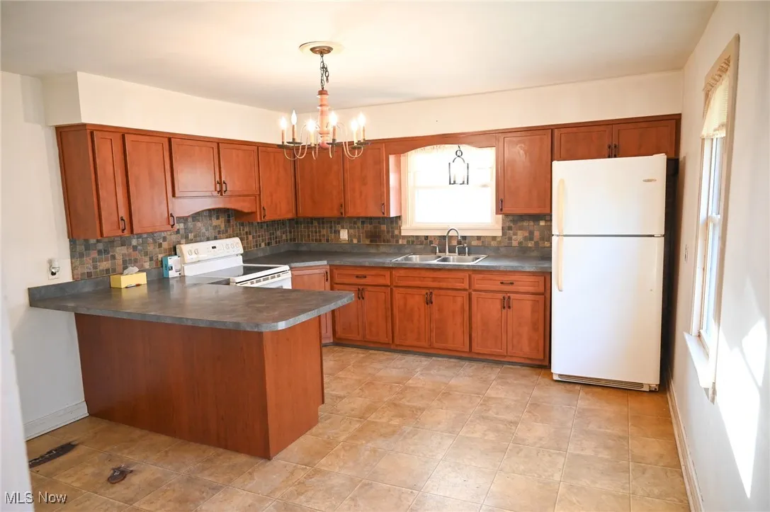 Kitchen with brown cabinets, decorative backsplash, white appliances, and dark countertops