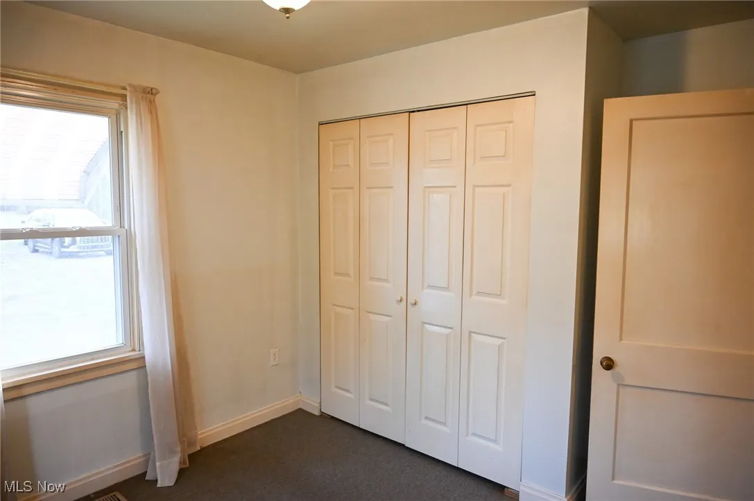 Unfurnished bedroom featuring multiple windows, a closet, and dark colored carpet