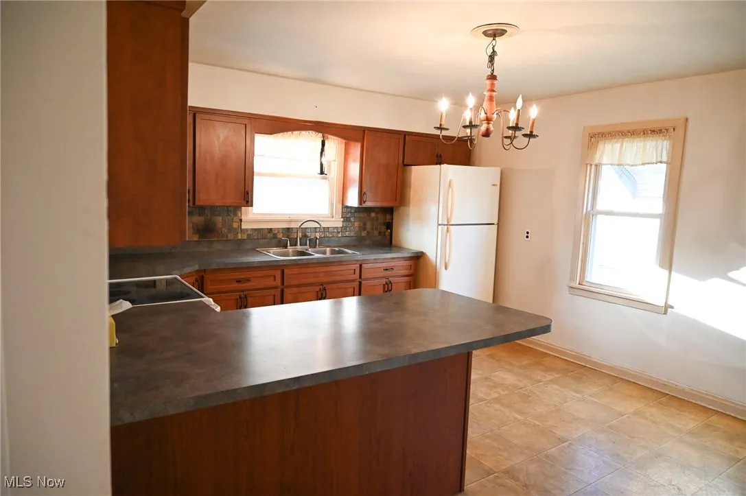 Kitchen with brown cabinets, tasteful backsplash, dark countertops, freestanding refrigerator, and a peninsula