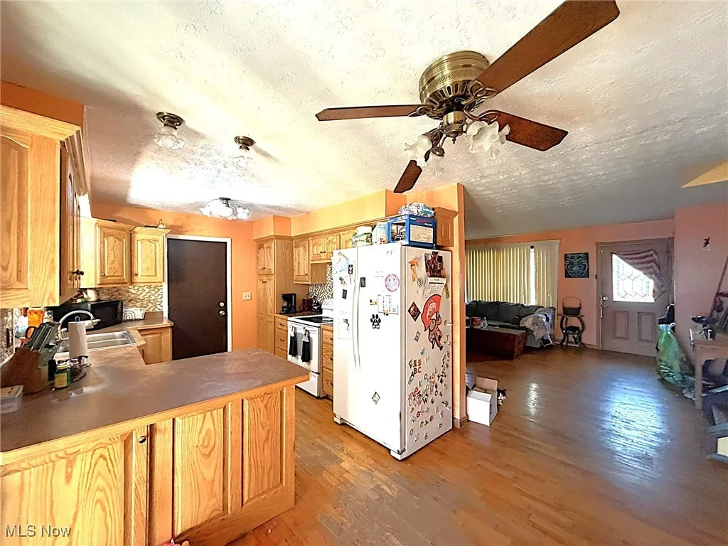 Kitchen with white appliances, light wood finished floors, a textured ceiling, backsplash, and a peninsula