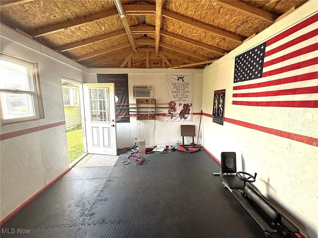 Workout area with vaulted ceiling, a wall mounted AC, and rubber floors