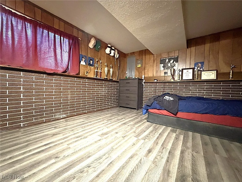 Bedroom with a textured ceiling, wood finished floors, and wooden walls