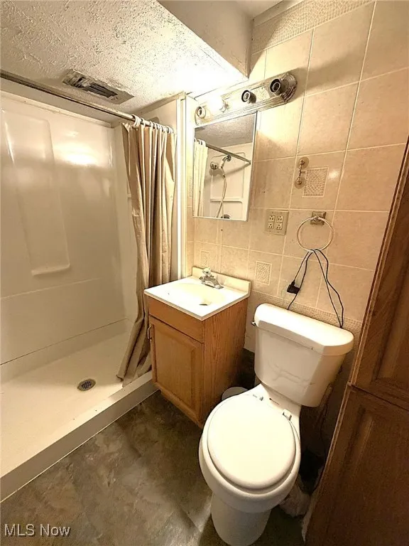 Bathroom featuring a stall shower, vanity, tile walls, a textured ceiling, and tasteful backsplash