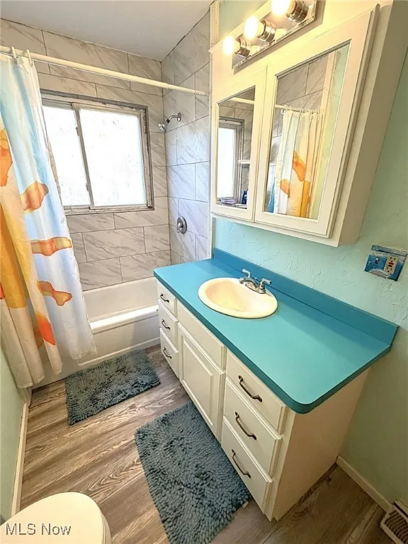 Bathroom with vanity, shower / tub combo with curtain, light wood finished floors, and a textured wall