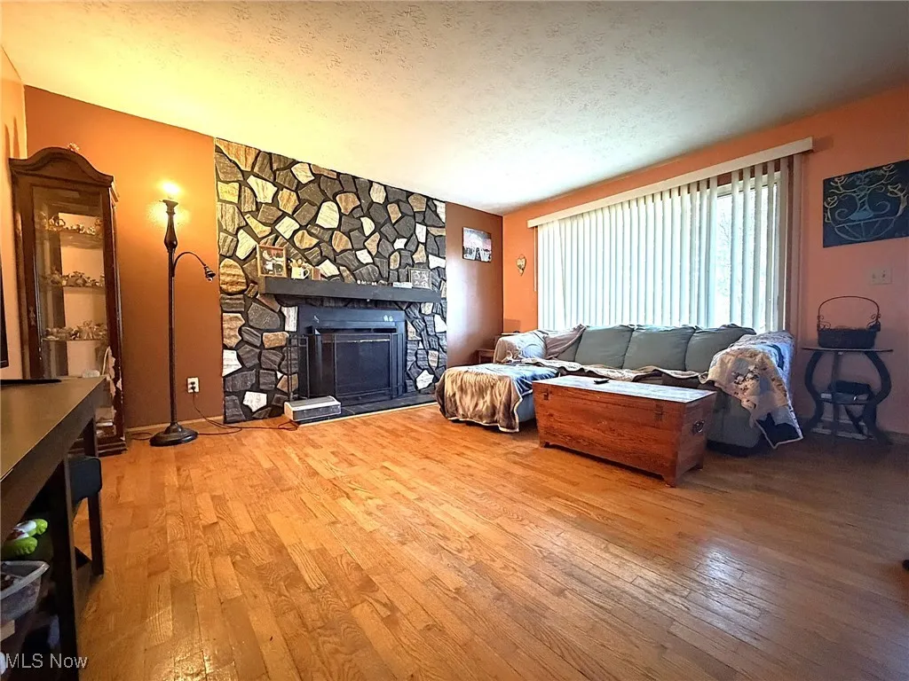 Living room featuring a textured ceiling, light wood-type flooring, and a stone fireplace