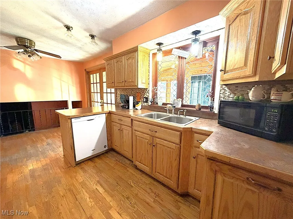 Kitchen with dishwasher, light wood-type flooring, black microwave, tasteful backsplash, and a peninsula