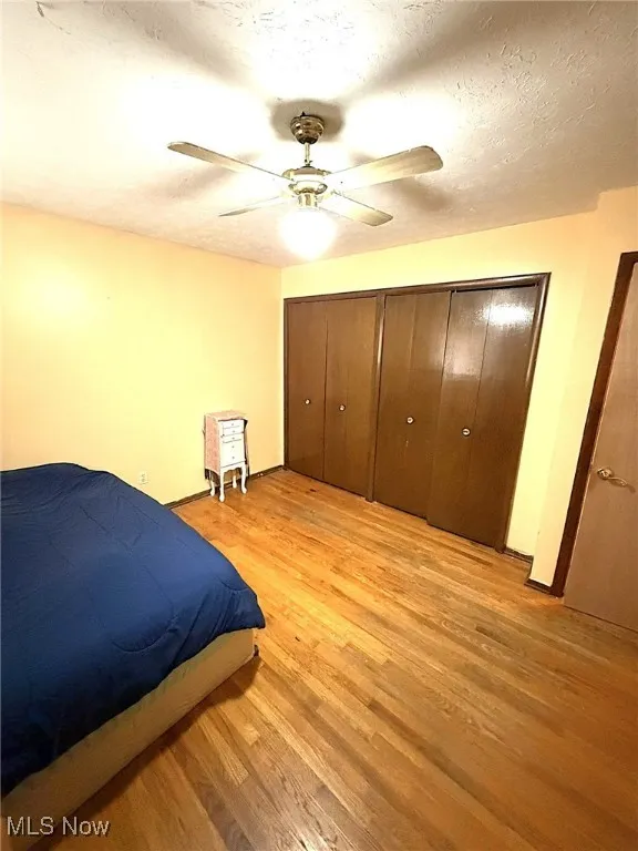Bedroom featuring a textured ceiling, light wood-type flooring, a ceiling fan, and a closet