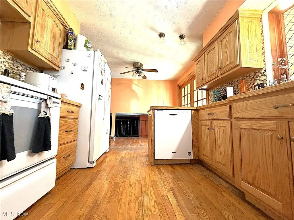 Kitchen with tasteful backsplash, white appliances, light wood finished floors, a peninsula, and a textured ceiling