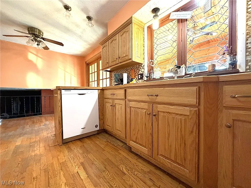 Kitchen with light wood-style flooring, dishwasher, a peninsula, a ceiling fan, and brown cabinets